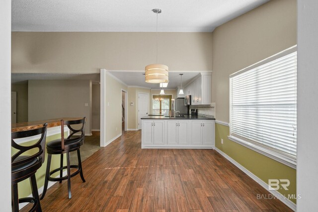7750 Charleston Oaks Dr, Daphne, AL 36526 - kitchen with white cabinets, dark countertops, hanging light fixtures, a peninsula, and dark wood-type flooring