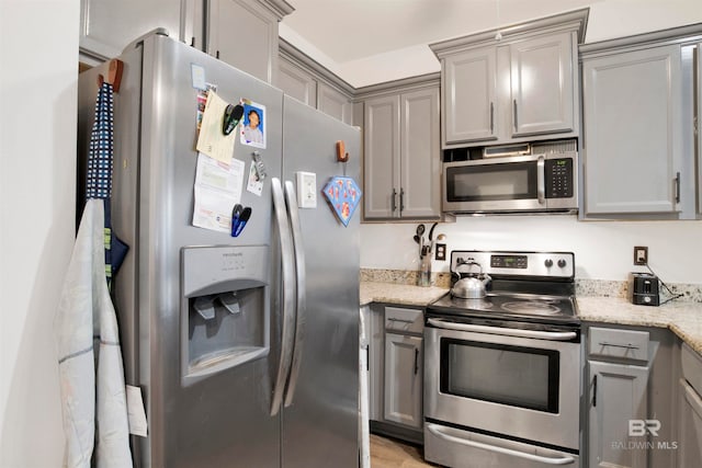 kitchen featuring gray cabinets, light stone countertops, and stainless steel appliances