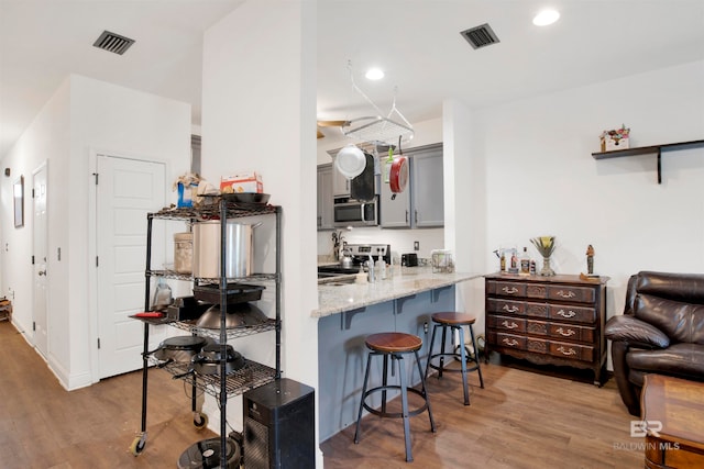 kitchen with light stone counters, hardwood / wood-style flooring, kitchen peninsula, gray cabinetry, and appliances with stainless steel finishes