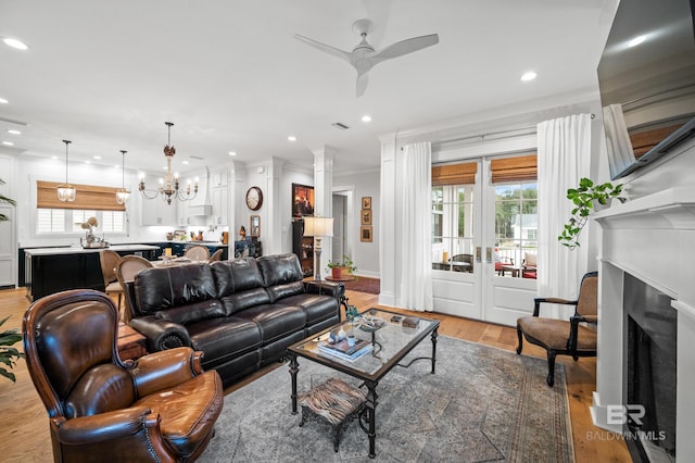 living room featuring ceiling fan with notable chandelier, light wood-type flooring, ornamental molding, and a wealth of natural light