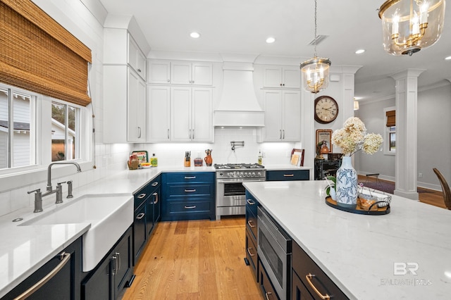 kitchen with pendant lighting, custom exhaust hood, white cabinets, appliances with stainless steel finishes, and decorative columns