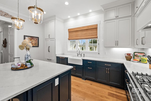 kitchen with white cabinetry, sink, decorative light fixtures, and light wood-type flooring