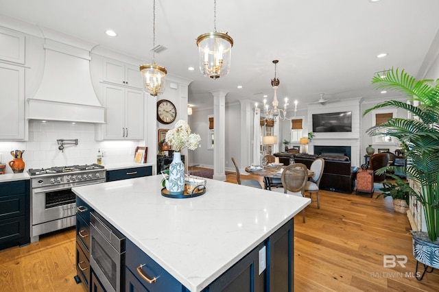 kitchen featuring appliances with stainless steel finishes, ornate columns, custom range hood, light hardwood / wood-style floors, and white cabinetry