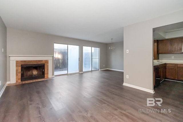 unfurnished living room featuring dark wood-style floors, baseboards, a chandelier, and a tiled fireplace