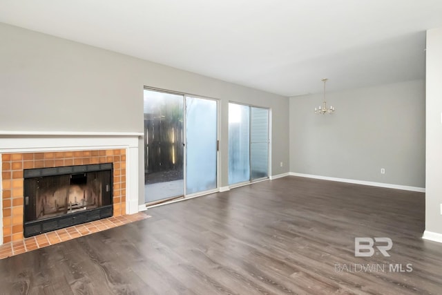 unfurnished living room with an inviting chandelier, baseboards, wood finished floors, and a tile fireplace