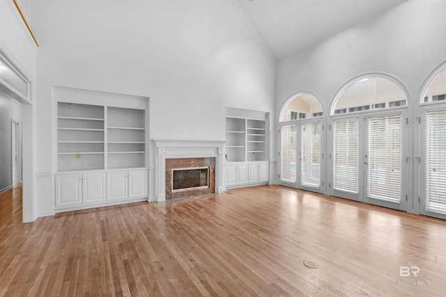 unfurnished living room with light wood-type flooring, a fireplace, high vaulted ceiling, and built in shelves