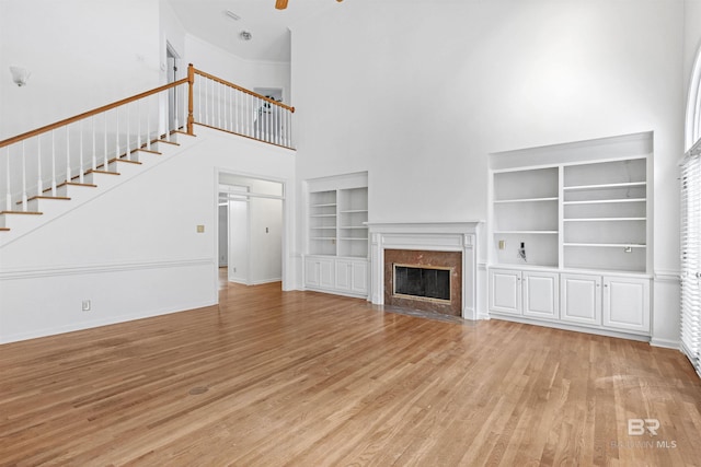 unfurnished living room with a high ceiling, ceiling fan, a fireplace, and light hardwood / wood-style floors