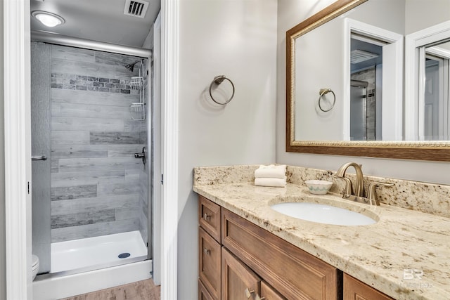 bathroom with hardwood / wood-style flooring, vanity, toilet, and tiled shower