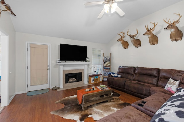 living room with baseboards, a tiled fireplace, a ceiling fan, wood finished floors, and vaulted ceiling