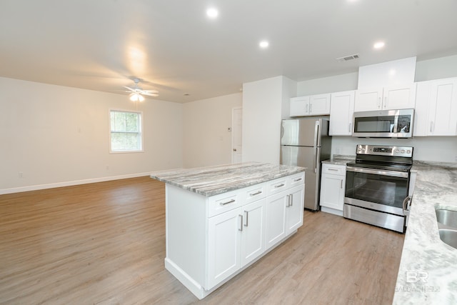 kitchen featuring appliances with stainless steel finishes, open floor plan, white cabinetry, light stone countertops, and light wood-type flooring