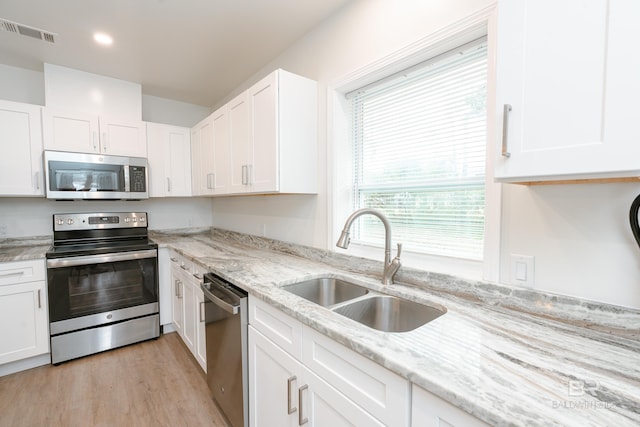 kitchen with white cabinetry, appliances with stainless steel finishes, light stone counters, and a sink