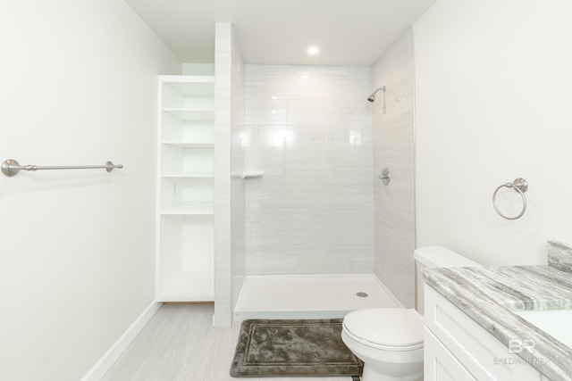 bathroom featuring baseboards, a tile shower, vanity, and toilet