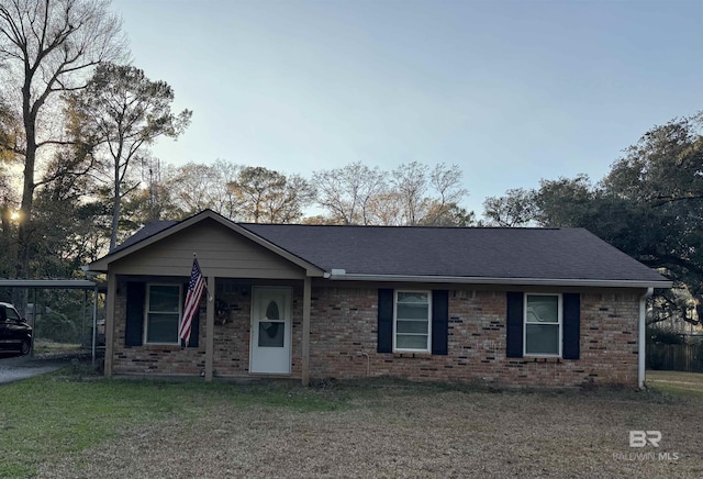 ranch-style home with a carport, brick siding, a front yard, and a shingled roof