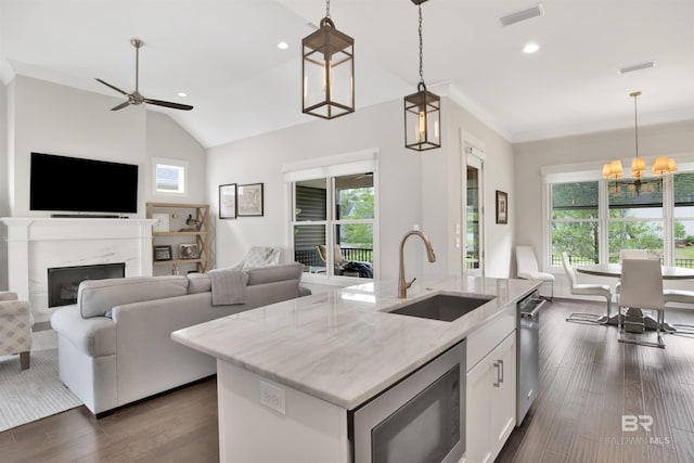 kitchen with white cabinets, light stone counters, decorative light fixtures, built in microwave, and a sink