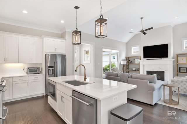 kitchen featuring light stone counters, stainless steel appliances, open floor plan, white cabinetry, and a sink