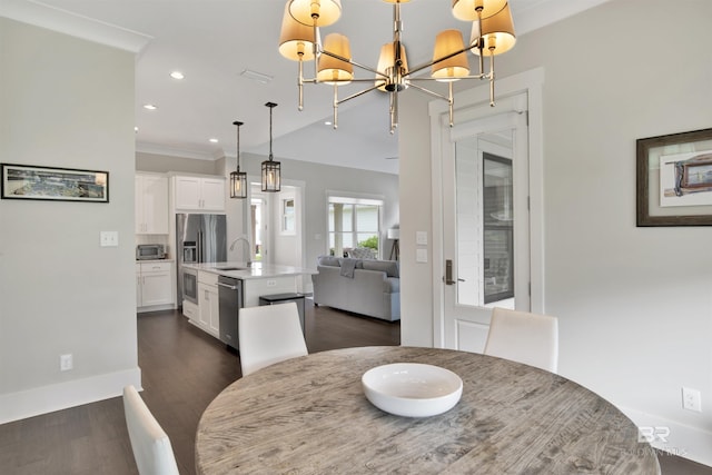 dining room featuring dark wood-type flooring, sink, a chandelier, and ornamental molding