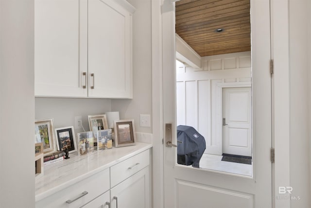 interior space with white cabinetry, light stone countertops, and wood ceiling