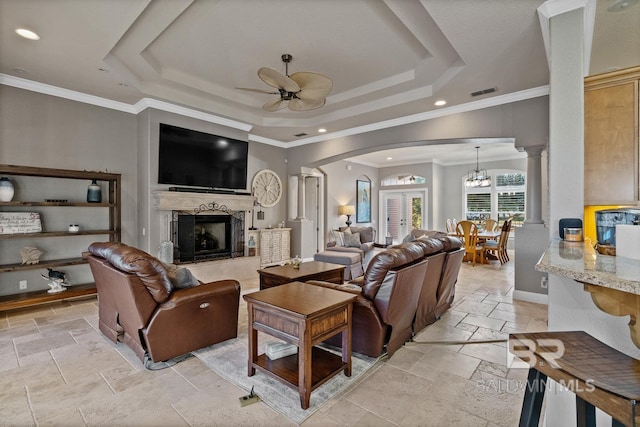 living room with ornate columns, ornamental molding, ceiling fan with notable chandelier, a raised ceiling, and a fireplace