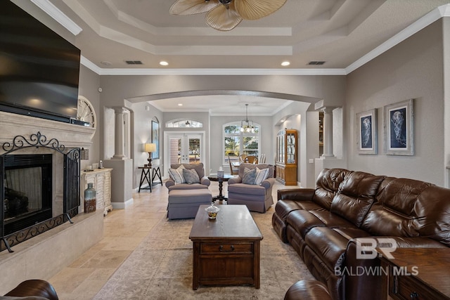 living room featuring ceiling fan with notable chandelier, ornamental molding, a tray ceiling, and ornate columns