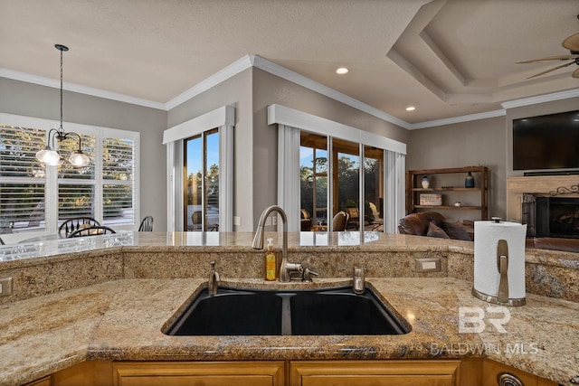 kitchen with light stone counters, sink, decorative light fixtures, and ornamental molding