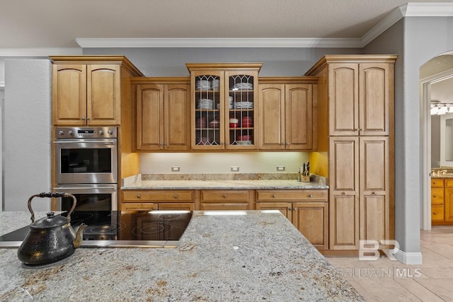 kitchen with crown molding, light tile patterned floors, a textured ceiling, light stone counters, and stainless steel double oven