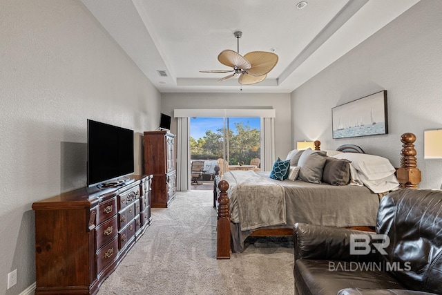 carpeted bedroom with a raised ceiling and ceiling fan