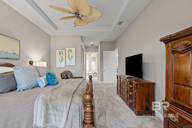 bedroom with light colored carpet, a raised ceiling, ceiling fan, and ensuite bathroom