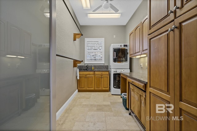 kitchen with stacked washing maching and dryer, ceiling fan, dark stone countertops, and sink