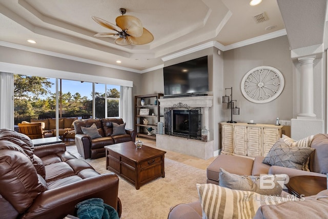 living room featuring a raised ceiling, ceiling fan, crown molding, and a premium fireplace