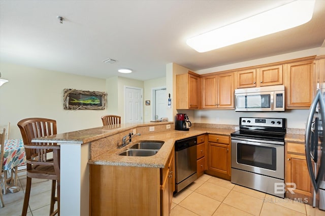 kitchen featuring a kitchen breakfast bar, appliances with stainless steel finishes, kitchen peninsula, sink, and light tile floors