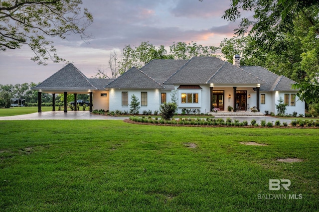 view of front facade featuring a chimney, french doors, a yard, concrete driveway, and an attached carport