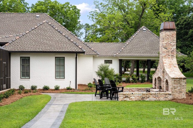 rear view of property featuring a patio, roof with shingles, a lawn, and a fireplace