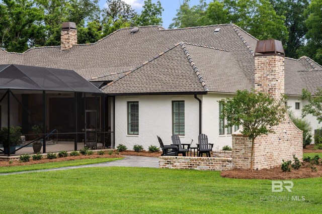 rear view of house with a chimney, a lanai, a yard, a patio, and a shingled roof