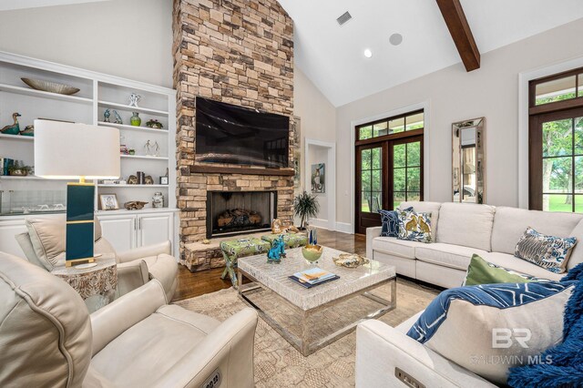living area featuring a stone fireplace, visible vents, wood finished floors, high vaulted ceiling, and beamed ceiling