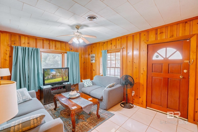 living room with tile patterned flooring, wooden walls, ceiling fan, and visible vents