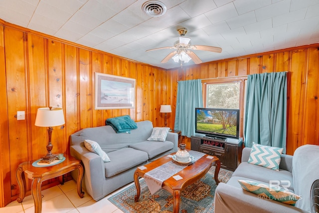 living room featuring light tile patterned flooring, visible vents, wood walls, and a ceiling fan