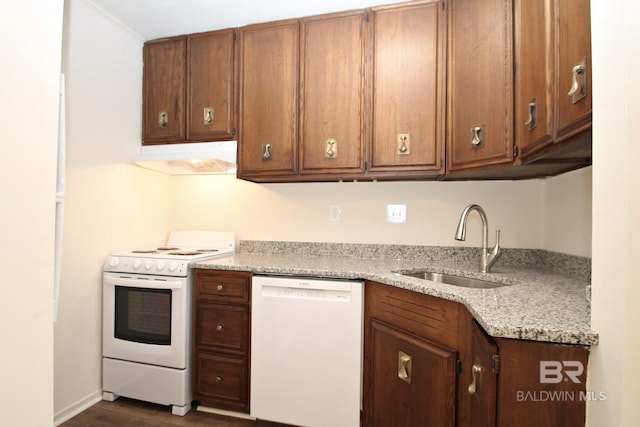 kitchen featuring white appliances, under cabinet range hood, brown cabinetry, and a sink