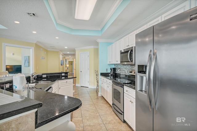 kitchen featuring stainless steel appliances, crown molding, a tray ceiling, white cabinets, and sink