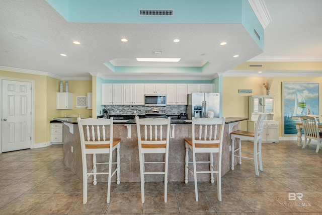 kitchen with white cabinets, ornamental molding, appliances with stainless steel finishes, a textured ceiling, and an island with sink