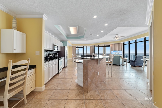 kitchen with crown molding, a tray ceiling, stainless steel appliances, a kitchen bar, and ceiling fan