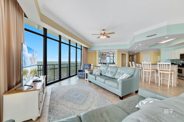 tiled living room featuring ornamental molding, ceiling fan, a raised ceiling, and a wall of windows