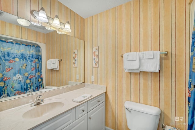 bathroom featuring vanity with extensive cabinet space, toilet, wooden walls, and a textured ceiling