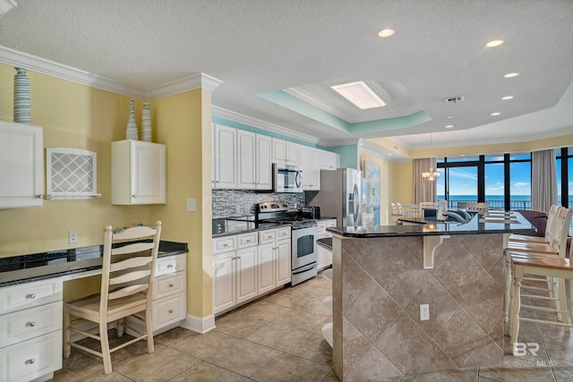 kitchen featuring a kitchen breakfast bar, light tile flooring, a tray ceiling, ornamental molding, and stainless steel appliances