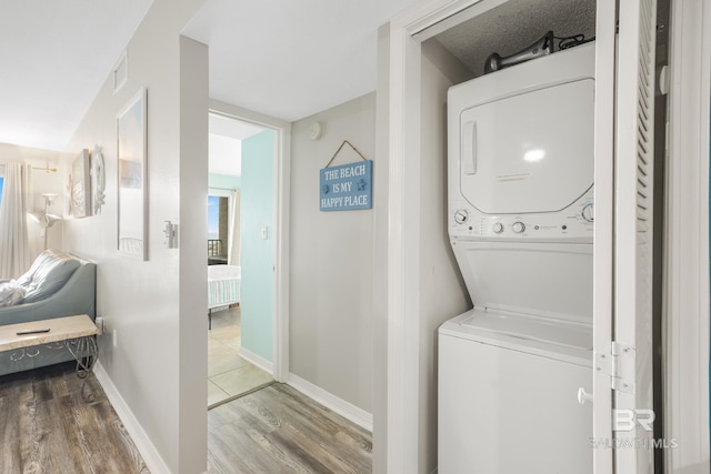 laundry room with visible vents, baseboards, laundry area, stacked washer / drying machine, and wood finished floors