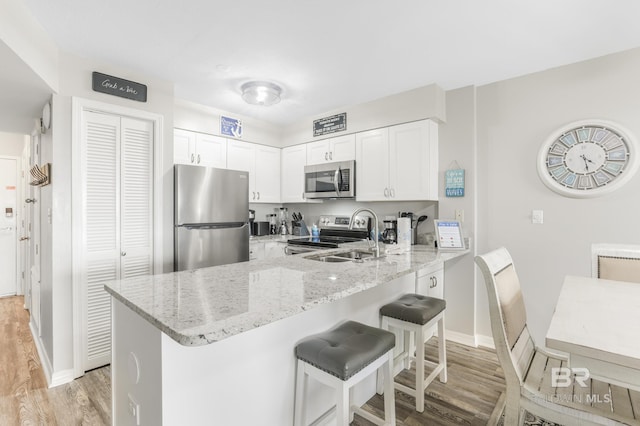 kitchen with a sink, a breakfast bar, appliances with stainless steel finishes, a peninsula, and light stone counters