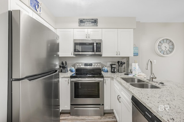 kitchen featuring white cabinets, a sink, light wood-type flooring, light stone countertops, and stainless steel appliances