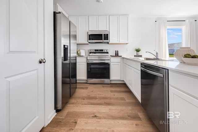 kitchen with light wood-type flooring, light countertops, white cabinets, a sink, and stainless steel appliances