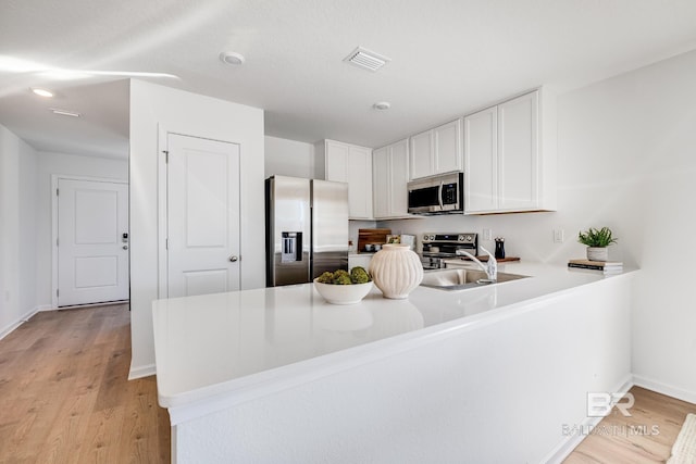 kitchen featuring a peninsula, light countertops, white cabinetry, light wood finished floors, and appliances with stainless steel finishes