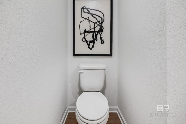 bathroom featuring baseboards, a textured wall, toilet, and wood finished floors