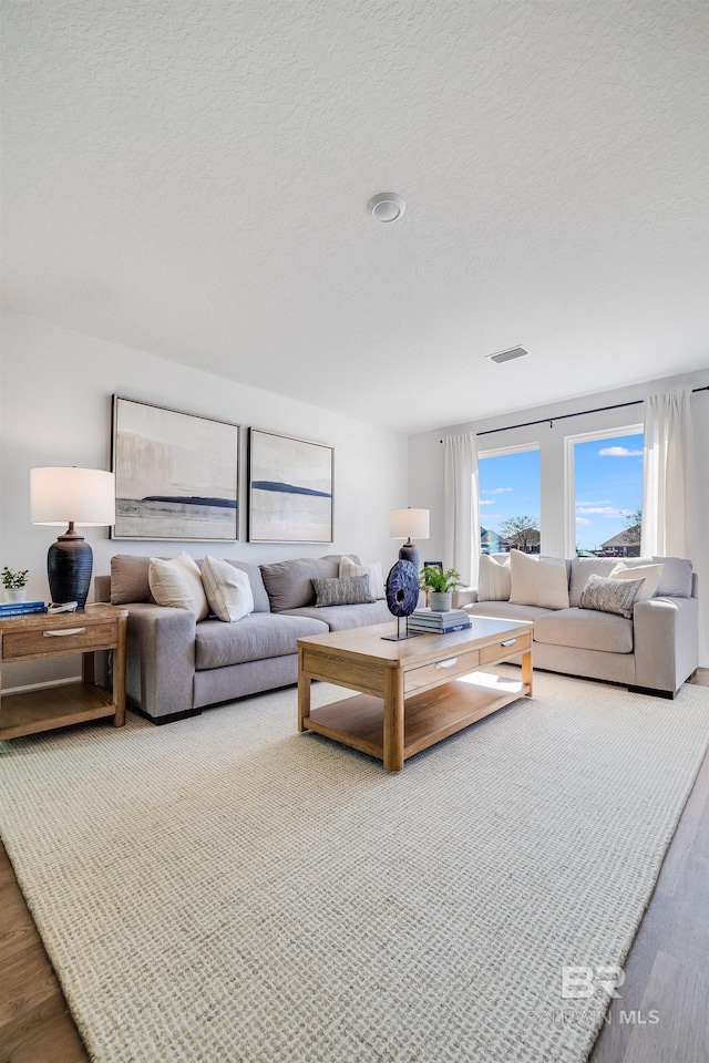 living area with a textured ceiling, visible vents, and wood finished floors